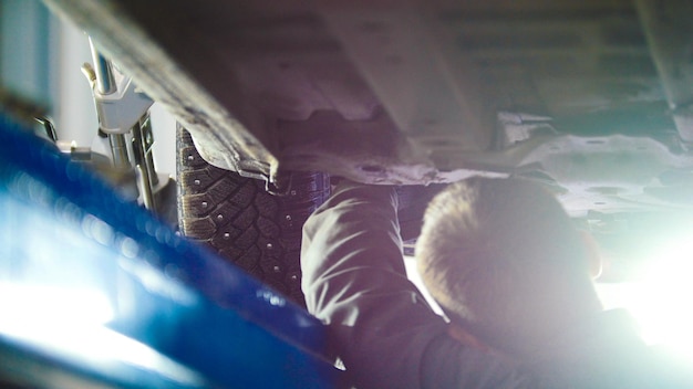 Auto service  mechanic unscrewing car parts while working under a lifted automobile