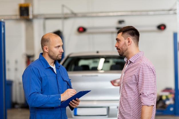 auto service, repair, maintenance and people concept - mechanic with clipboard talking to man or owner at car shop