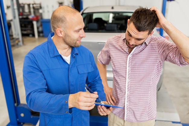 auto service, repair, maintenance and people concept - mechanic with clipboard talking to man or owner at car shop