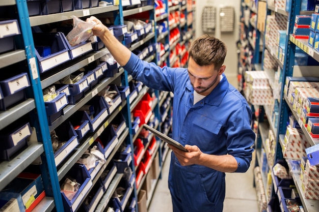 auto service, reparatie, onderhoud en mensen concept - automonteur man of smid met tablet pc computer op zoek naar reserveonderdelen in werkplaats of magazijn