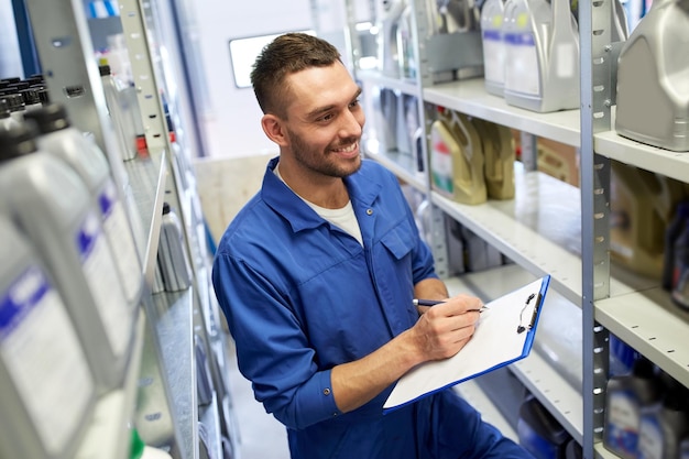 auto service, reparatie, onderhoud en mensen concept - lachende automonteur man of smith schrijven naar klembord in werkplaats of magazijn