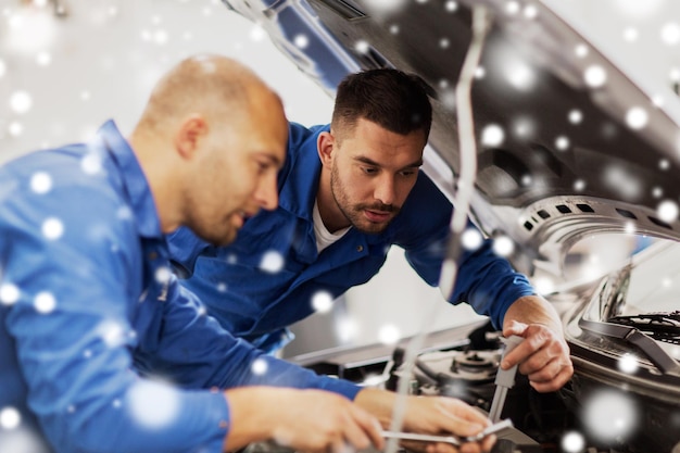 Auto-service reparatie onderhoud en mensen concept monteur mannen met sleutel reparatie auto in de werkplaats over sneeuw