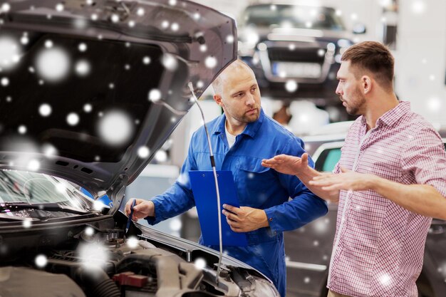 Foto auto-service reparatie onderhoud en mensen concept monteur met clipboard en man of eigenaar praten bij auto-winkel over sneeuw