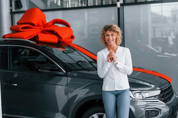 Foto auto staat met cadeau lengte bovenaan vrouw met blond krullend haar staat in autosalon