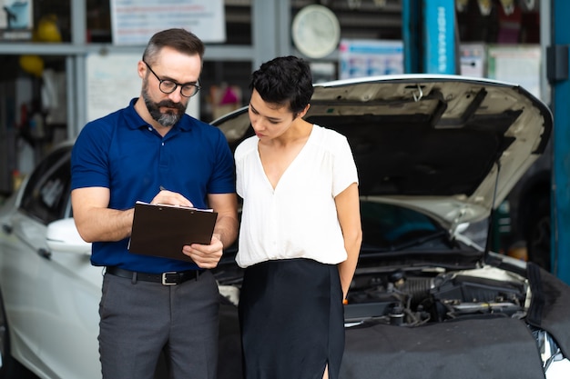 Auto verzekering concept. Verzekeringsagent onderzoekt beschadigde auto met vrouwelijke klant en schrijft informatie op het claimformulier.