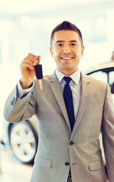 autobedrijf, autoverkoop, consumentisme en mensenconcept - gelukkige man die sleutel toont op autoshow of salon