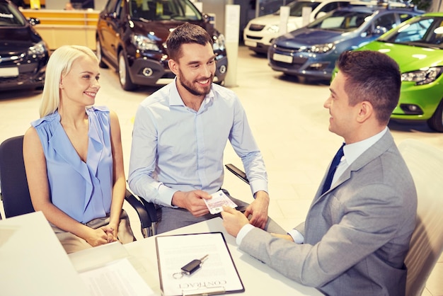 Foto autobedrijf, verkoop en mensenconcept - gelukkig paar met dealer die auto koopt in autoshow of salon