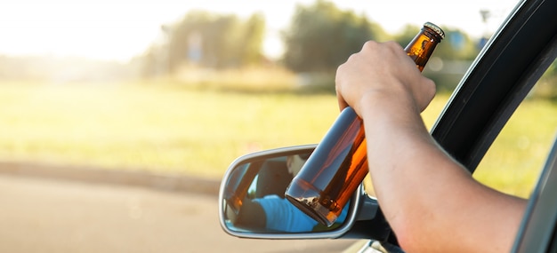 Autobestuurder die een fles bier houdt