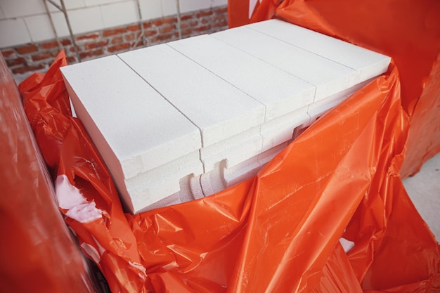 Автоклавные газоблоки на бетонном фундаменте процесс строительства дома Стопки белых газоблоков для укладки на бетонный фундамент Стройматериалы на строительной площадке