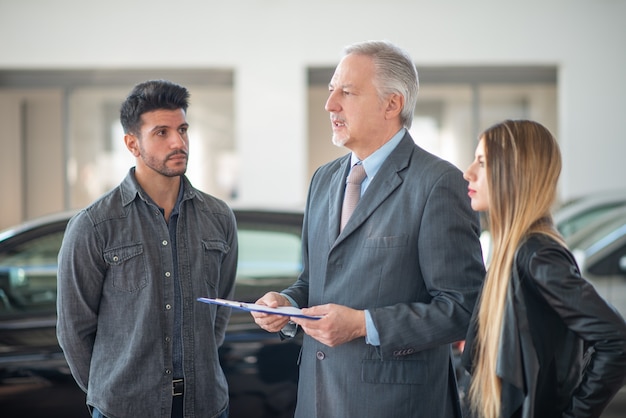 Autodealer die de kenmerken van een auto uitlegt aan een stel door een document te lezen