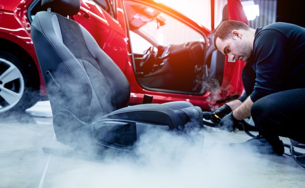 Autodienstmedewerker autostoel schoonmaken met een stoomreiniger