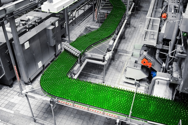 Automated conveyor line in a brewery. Rows of green glass bottles on a conveyor belt.