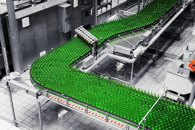 Photo automated conveyor line in a brewery. rows of green glass bottles on a conveyor belt.