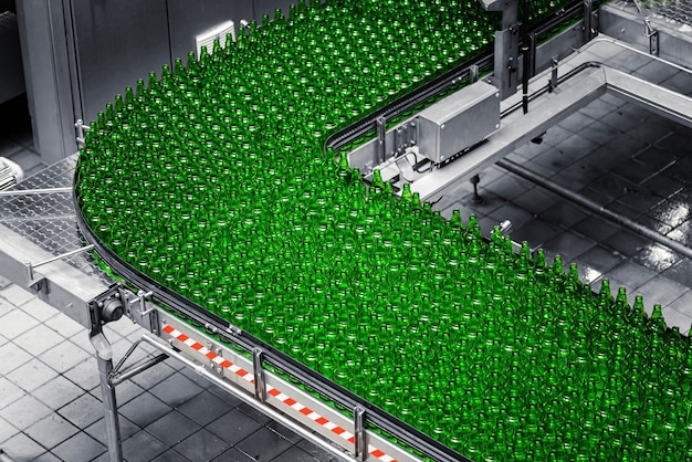 사진 양조장의 자동화 된 컨베이어 라인. 컨베이어 벨트에 녹색 유리 병의 행.
