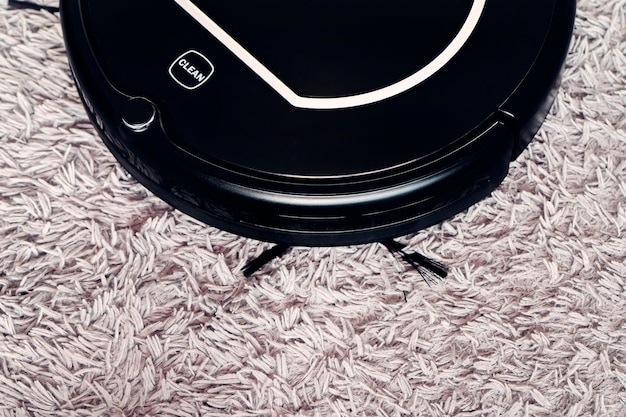 Automatic robot vacuum cleaner in black on a gray shag carpet. New modern technologies for apartment cleaning. smart home electronic assistant