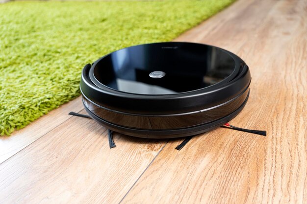 Automatic robot vacuum cleaner in black on green shag carpet New modern technologies for apartment cleaning smart home electronic assistant