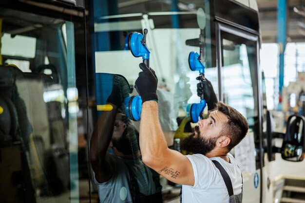 An automechanic worker adjusting new windows on the bus while standing in the workshop