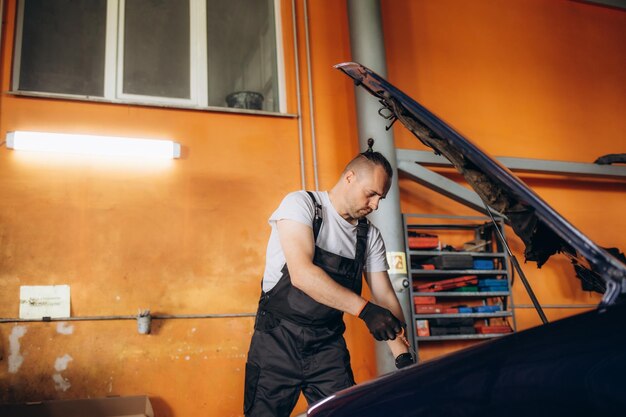 Automechanicus werkt onder de kap in de garage.