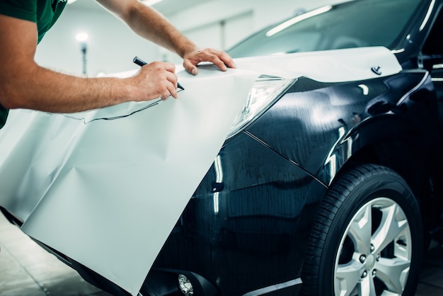 Processo di installazione della pellicola protettiva per vernice automobilistica. le mani dell'operaio si preparano a proteggere il rivestimento da scheggiature e graffi