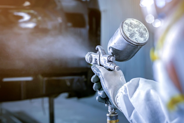 Foto pittore di automobili in abiti da lavoro protettivi e carrozzeria di verniciatura del respiratore nella camera di verniciatura