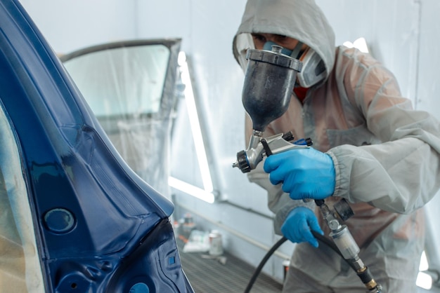 Automobile repairman painter hand in protective glove with airbrush pulverizer painting car body in paint chamber.