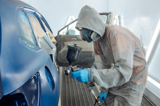 Automobile repairman painter hand in protective glove with airbrush pulverizer painting car body in