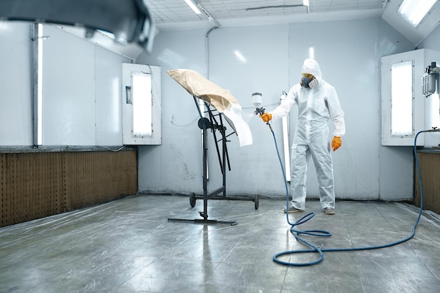 Automobile repairman using airbrush pulverizer for painting car door body part in workshop chamber