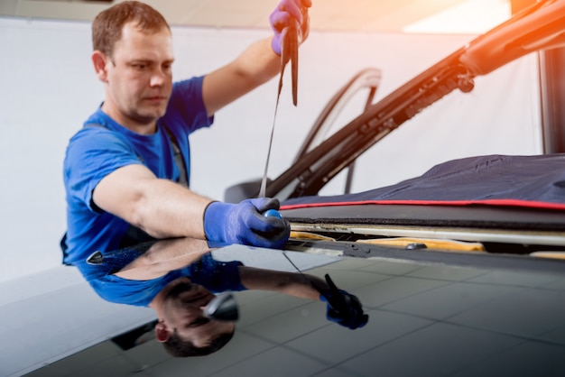 Automobile special workers remove old windscreen or windshield of a car in auto service station garage.