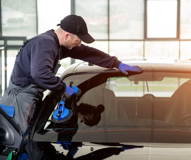 Photo automobile special workers replacing windscreen or windshield of a car in auto service station garage.