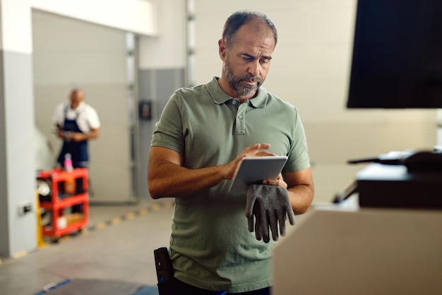 Automonteur bezig met digitale tablet bij reparatiewerkplaats