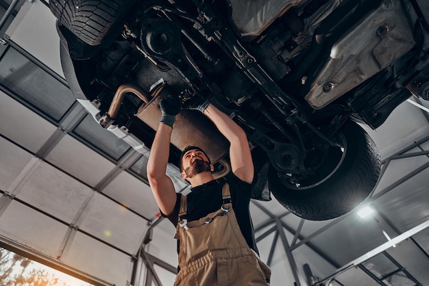 Automonteur die autowiel en ophangingsdetail van opgeheven autoreparatieservicestation inspecteert