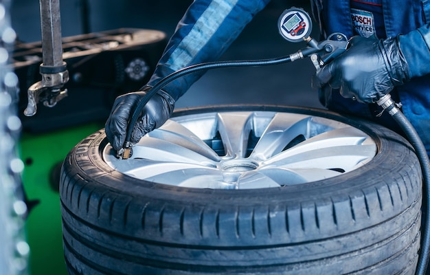 Automonteur die de bandenspanning van de auto controleert op het verwijderde wiel in de autoservicegarage