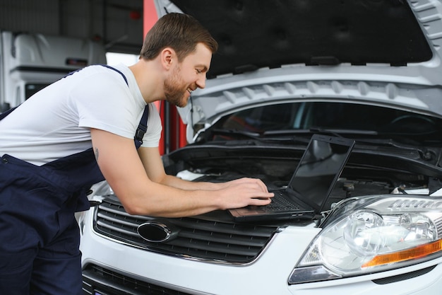 Automonteur die een computerlaptop gebruikt voor het diagnosticeren en controleren van onderdelen van automotoren voor reparatie en reparatie