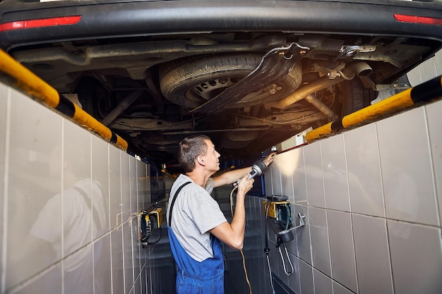 Automonteur die het loopwerk van de auto controleert op het tankstation Mannelijke werknemer die het probleem met het auto-onderhoudsconcept oplost