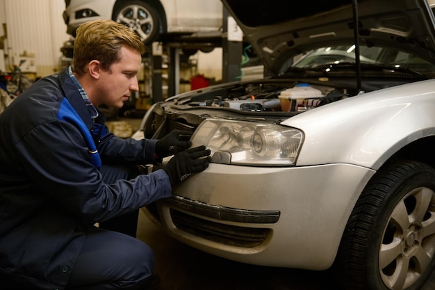 Automonteur in autoservice die koplampen op auto in de garage van de reparatiewerkplaats aanpast. Autoservice, autoreparatie en garantie-onderhoudsconcept