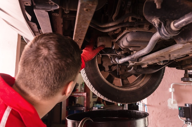 Automonteur in uniform aan het werk onder een opgeheven auto met werkuitrusting