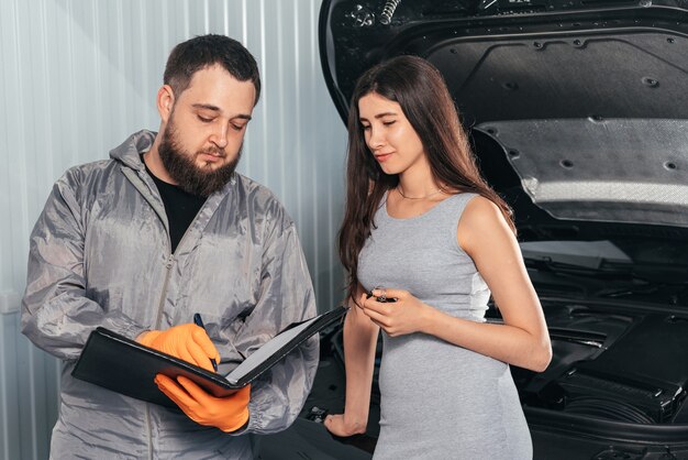 Automonteur legt de reparatiefactuur van het voertuig uit aan vrouwelijke klant en ondertekent papieren