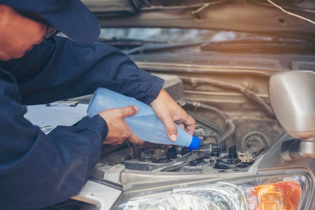 Foto automonteur man handen gieten gedeïoniseerd gezuiverd gedestilleerd water voor auto batterij mechanische service close-up handen man houden gedeïoniseerd gedistilleerde vloeibare waterfles bij garage auto mobiele auto service