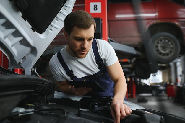 Automonteur met behulp van digitale tablet met service- en onderhoudsapp op het scherm tijdens het inspecteren van het voertuig in de autoreparatiewerkplaats