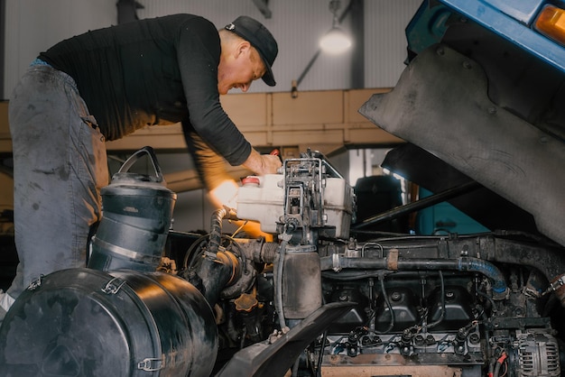 Automonteur repareert grote vrachtwagen of tractor in werkplaats Professionele monteur repareert vrachtwagenmotor Echte werknemer