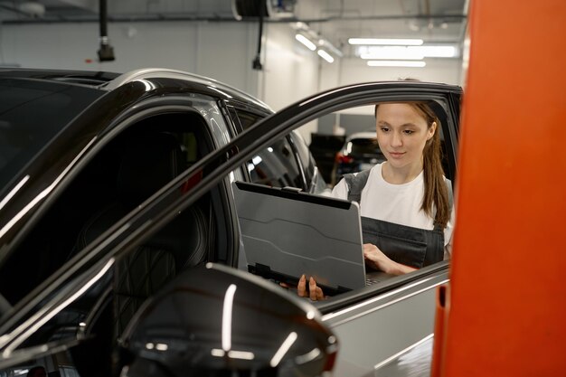 Automonteur van de vrouw die het probleem van het repareren van de auto van de klant controleert met behulp van laptop voor diagnostiek in de reparatiewerkplaats