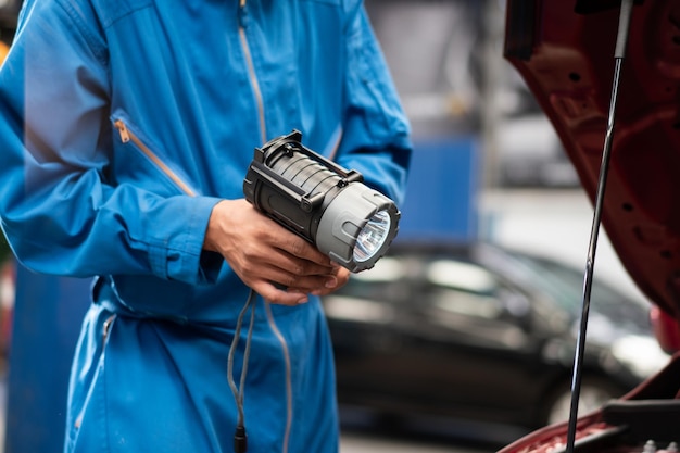 Automotive mechanic holding flashlight preparing for repairing car at auto garage shop