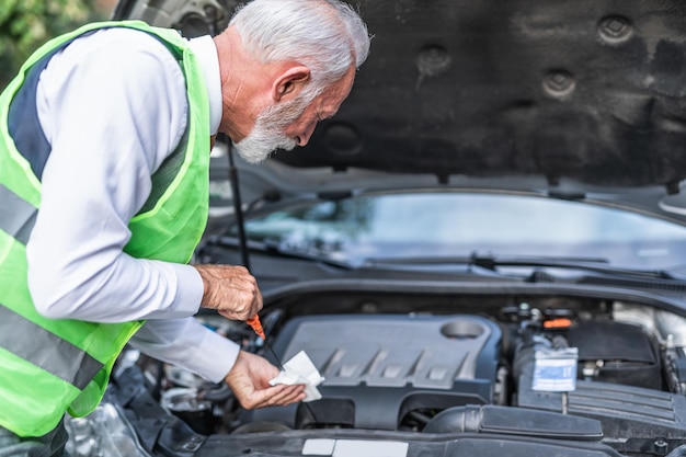 Autopech. Bezorgde senior man kijkt naar de motor van een auto en probeert deze te repareren.