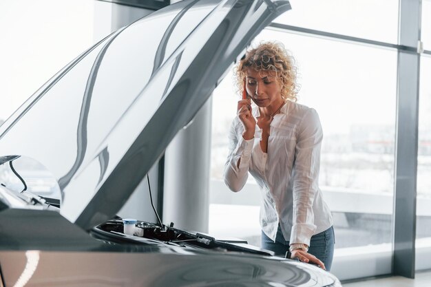 Foto autopech vrouw met blond krullend haar staat in autosalon