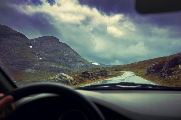 Autorijden op bergweg Weg tussen bergen met dramatische stormachtige bewolkte hemel Prachtige natuur Noorwegen Zonsondergang