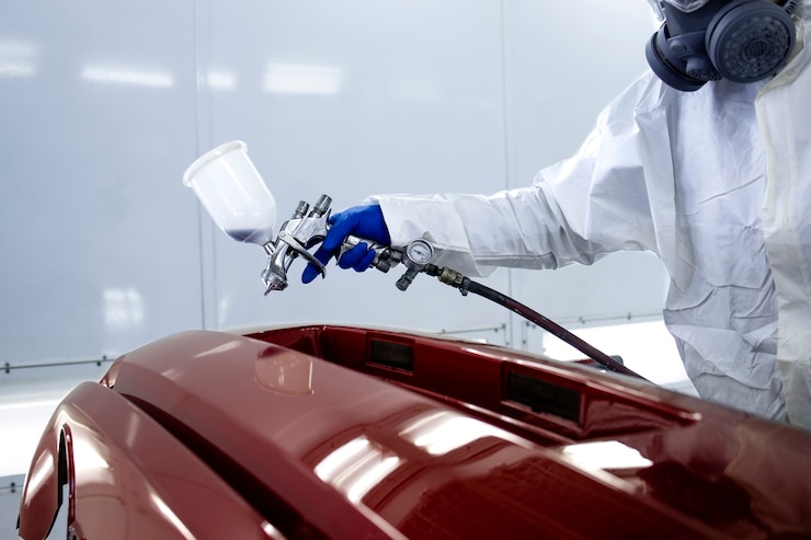 Autoschilder in beschermende kleding en masker auto bumper met metallic verf en lak in kamer werkplaats schilderen.