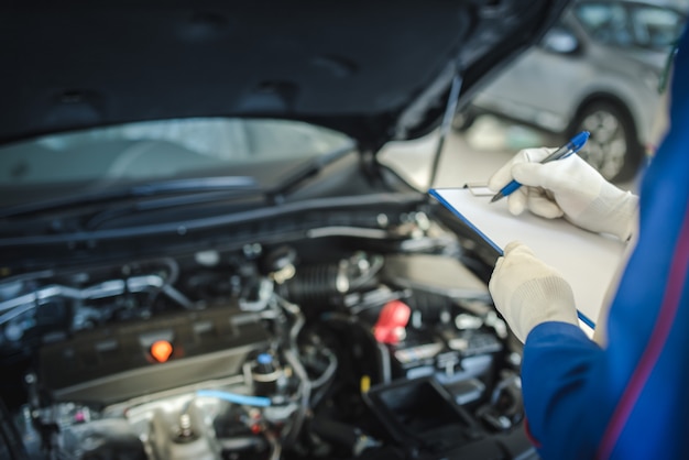 Autoservice, reparatie, onderhoudsconcept - Aziatische automonteur man of Smith schrijven naar het klembord in werkplaats of magazijn, technicus doet de checklist voor reparatiemachine voor een nieuwe auto