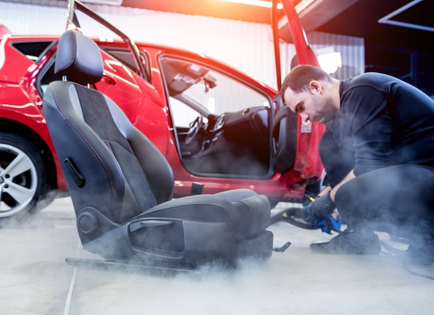 Autoservicemedewerker die autostoel schoonmaakt met een stoomreiniger