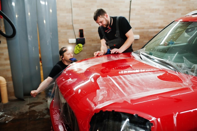 Autoservicemedewerker plaatste anti-grindfilm op een rode carrosserie bij de detailleringsvoertuigwerkplaats Autobescherming met speciale films