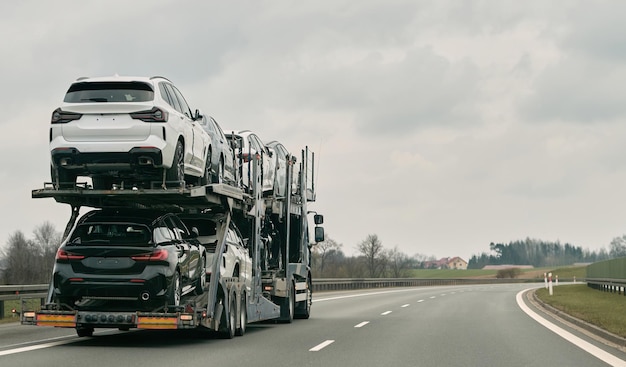 Autotransporter vervoert nieuwe luxe voertuigen langs de snelweg achteraanzicht van de aanhangwagen Grote autotransportwagen van nieuwe sport Duitse auto's levering aan dealer vrachtwagen van nieuwe krachtige nieuwe voertuigen